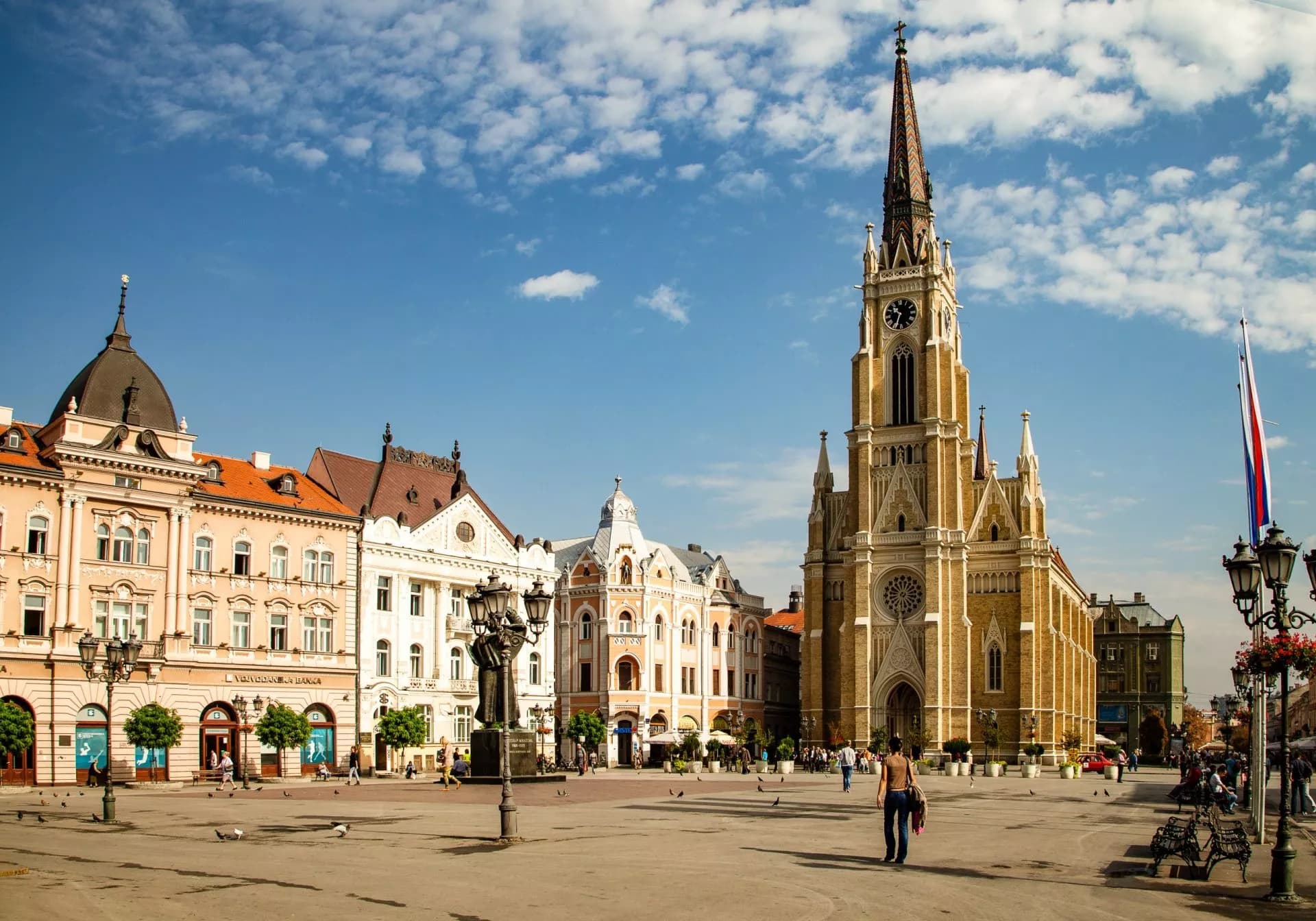 Novi Sad city square with Name of Mary Church and historic buildings under blue sky.