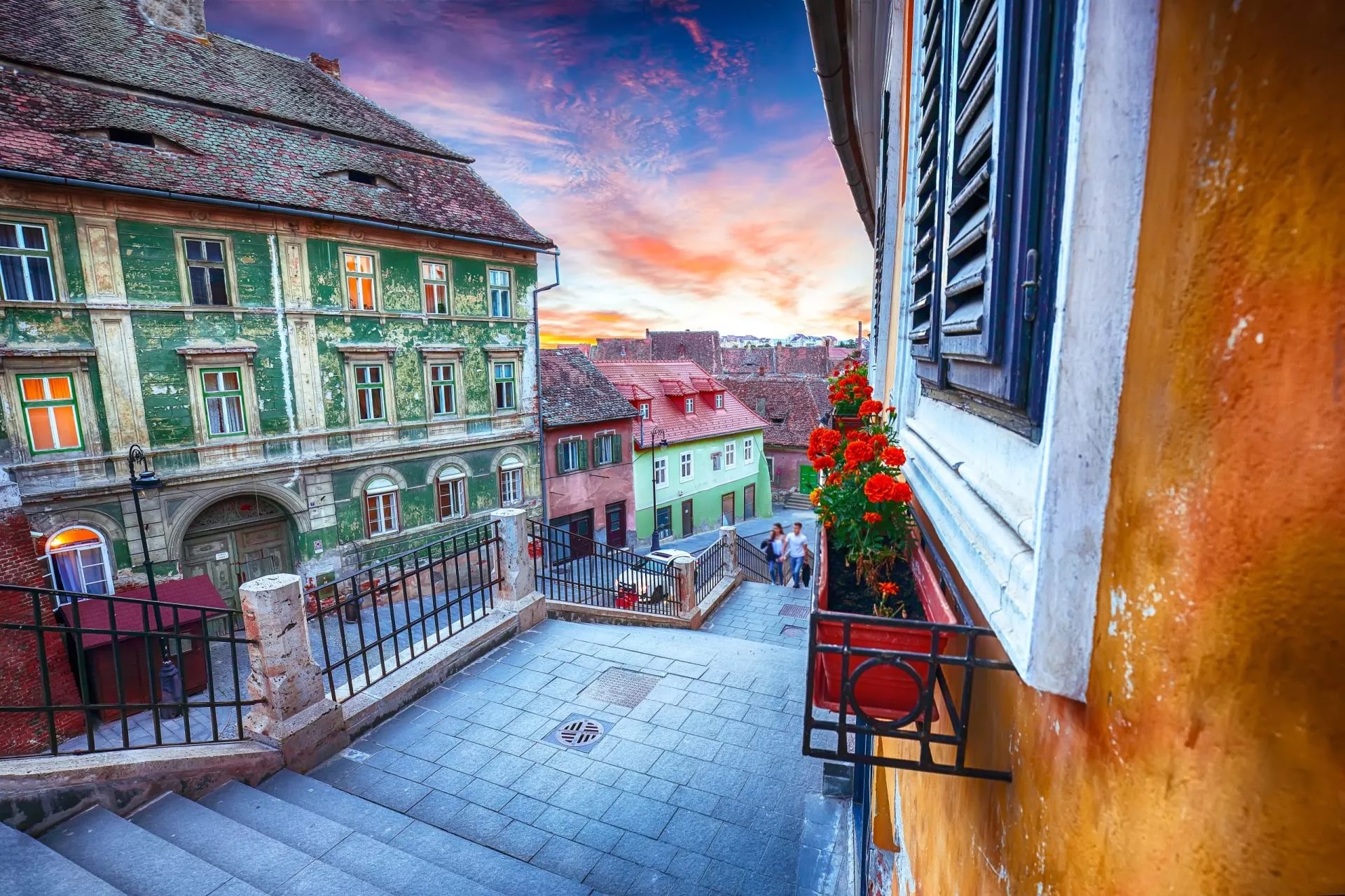 Stone steps descending in Sibiu, Romania, past colorful buildings at sunset.
