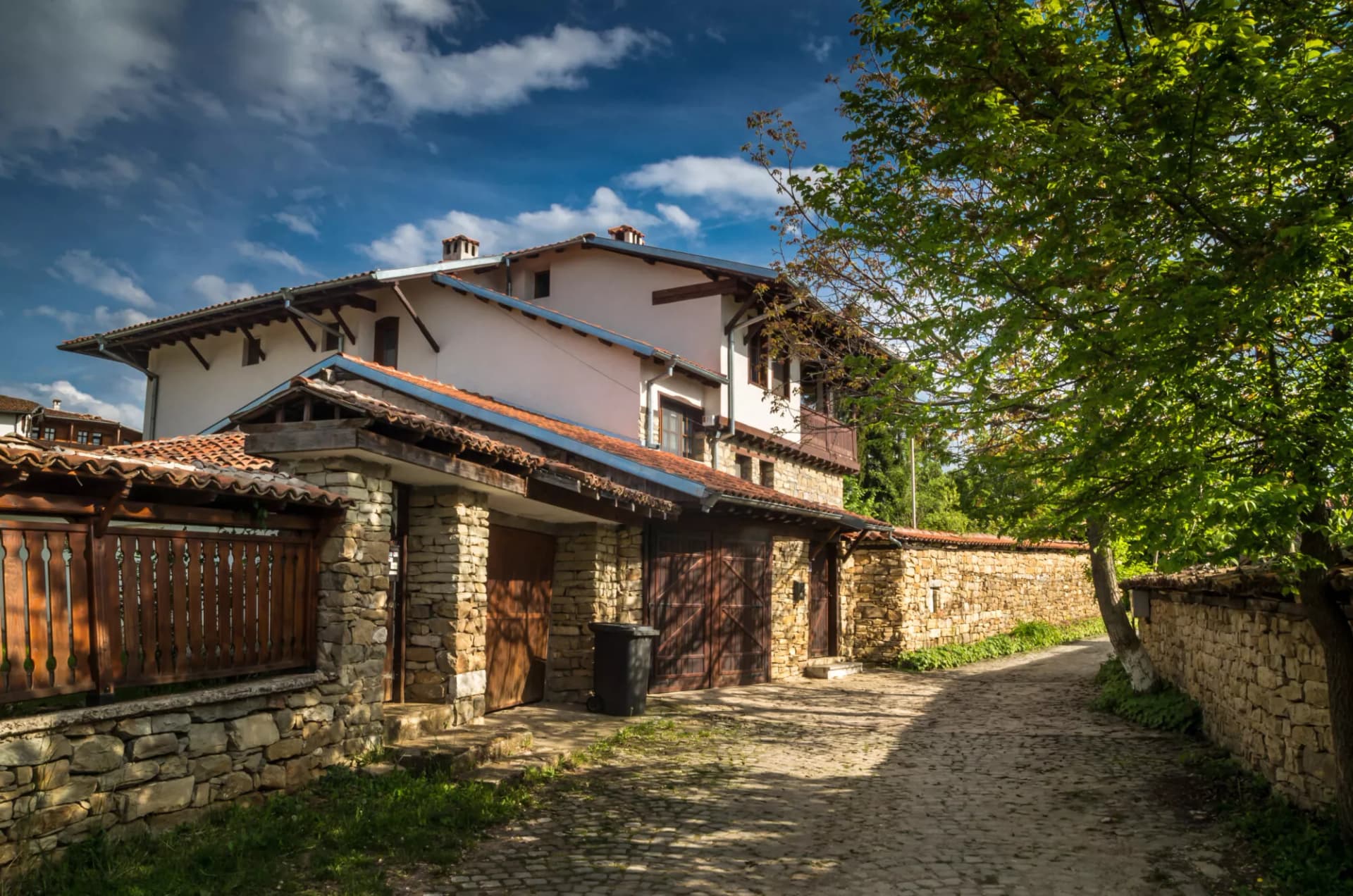 Stone house with tile roof and wooden fence along a cobblestone path in Arbanasi.