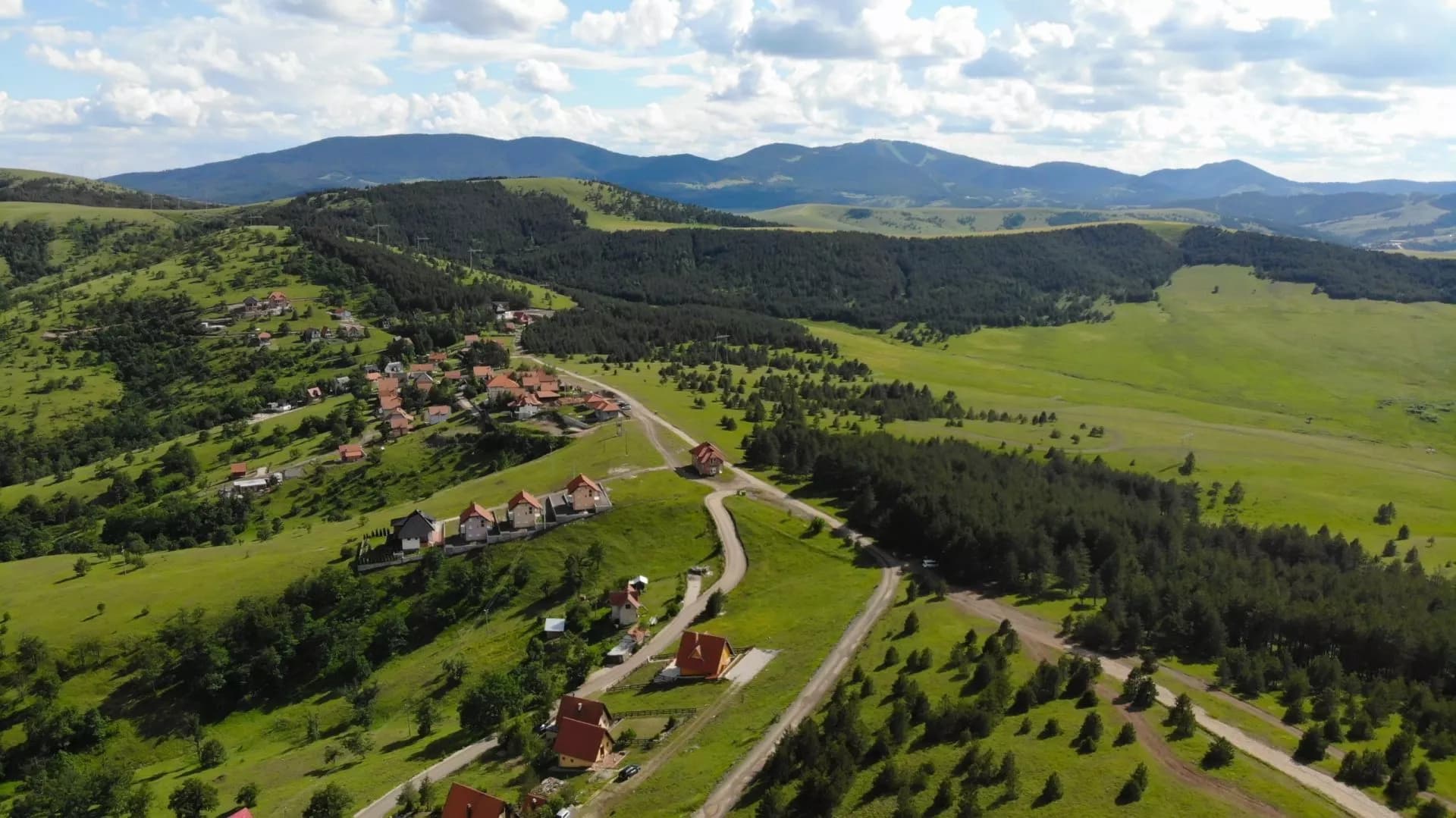 Village houses on green rolling hills with pine forests and mountains in Zlatibor, Serbia.