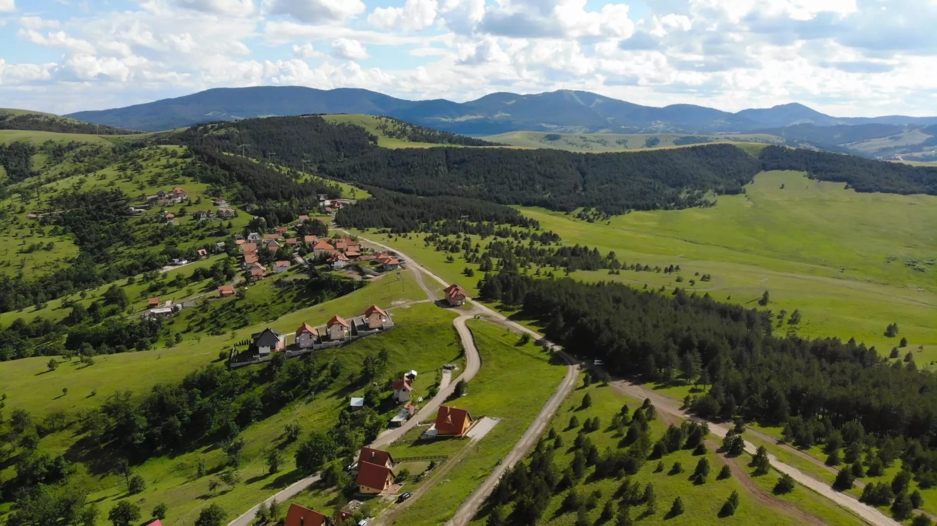 Mountain village with red-roofed houses nestled in green rolling hills under a cloudy sky in Zlatibor, Serbia.
