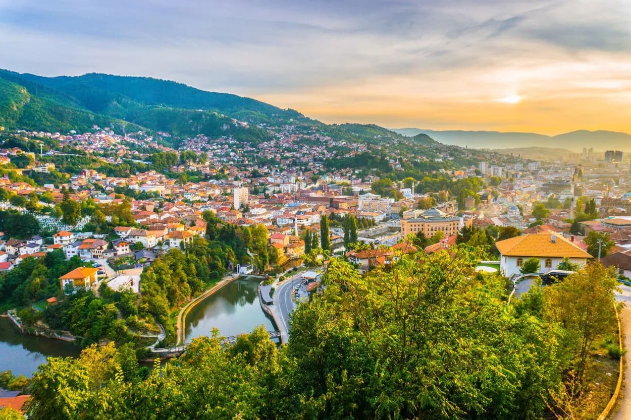 Aerial view of Sarajevo city nestled in green mountains at sunset with a river winding through.