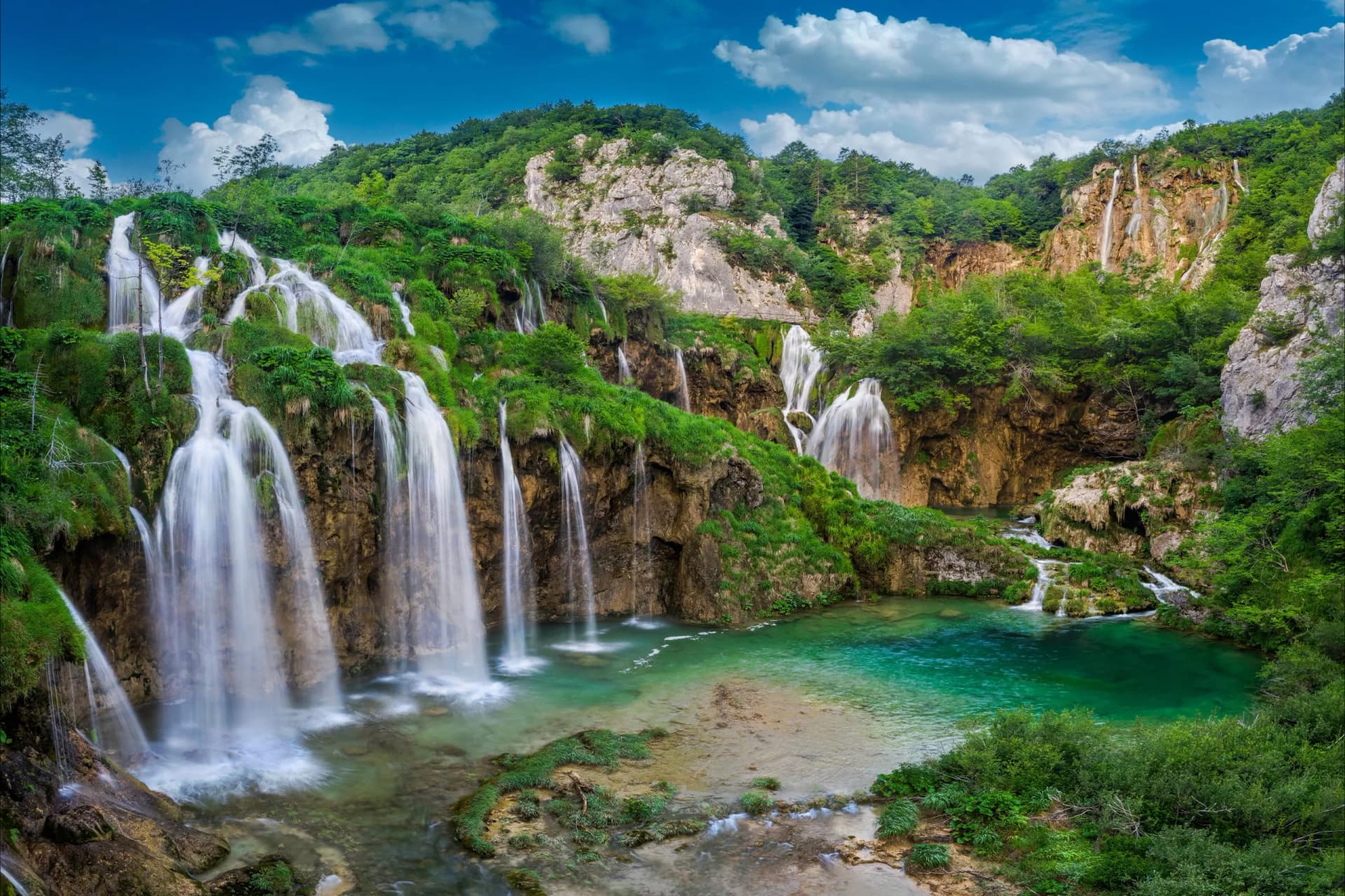 Waterfalls cascade over mossy cliffs into turquoise pools at Plitvice Lakes National Park, Croatia.