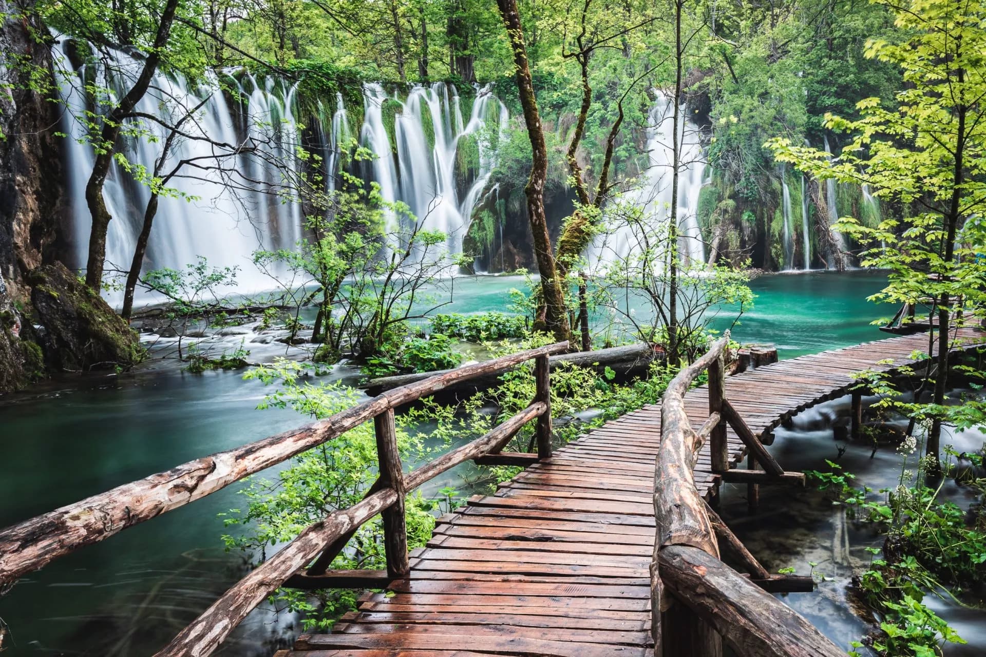 Boardwalk walking around Plitvice Lakes on a rainy day with waterfalls and turquoise water.
