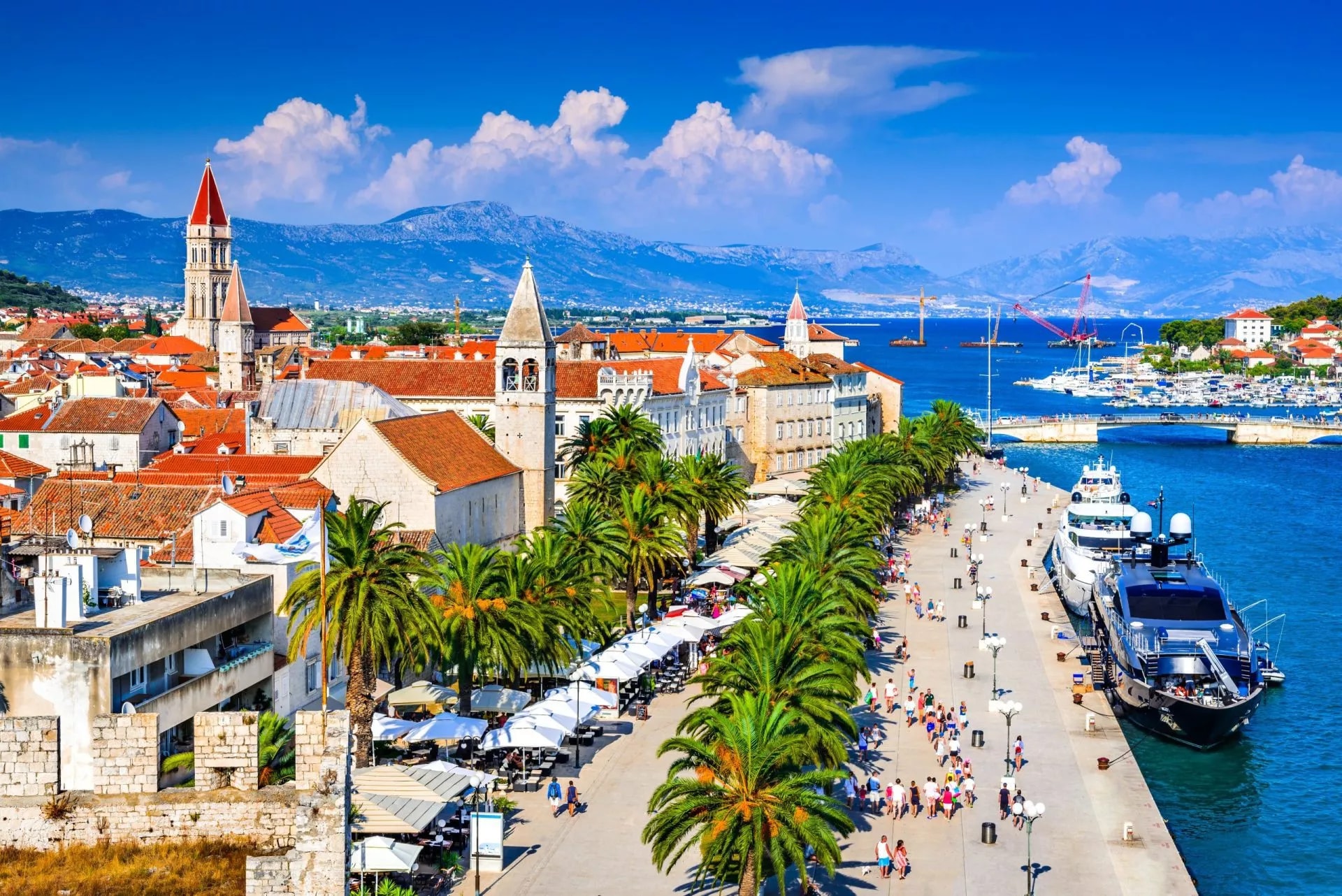 Trogir waterfront with palm trees, historic buildings, and yachts in the Dalmatia region of Croatia.