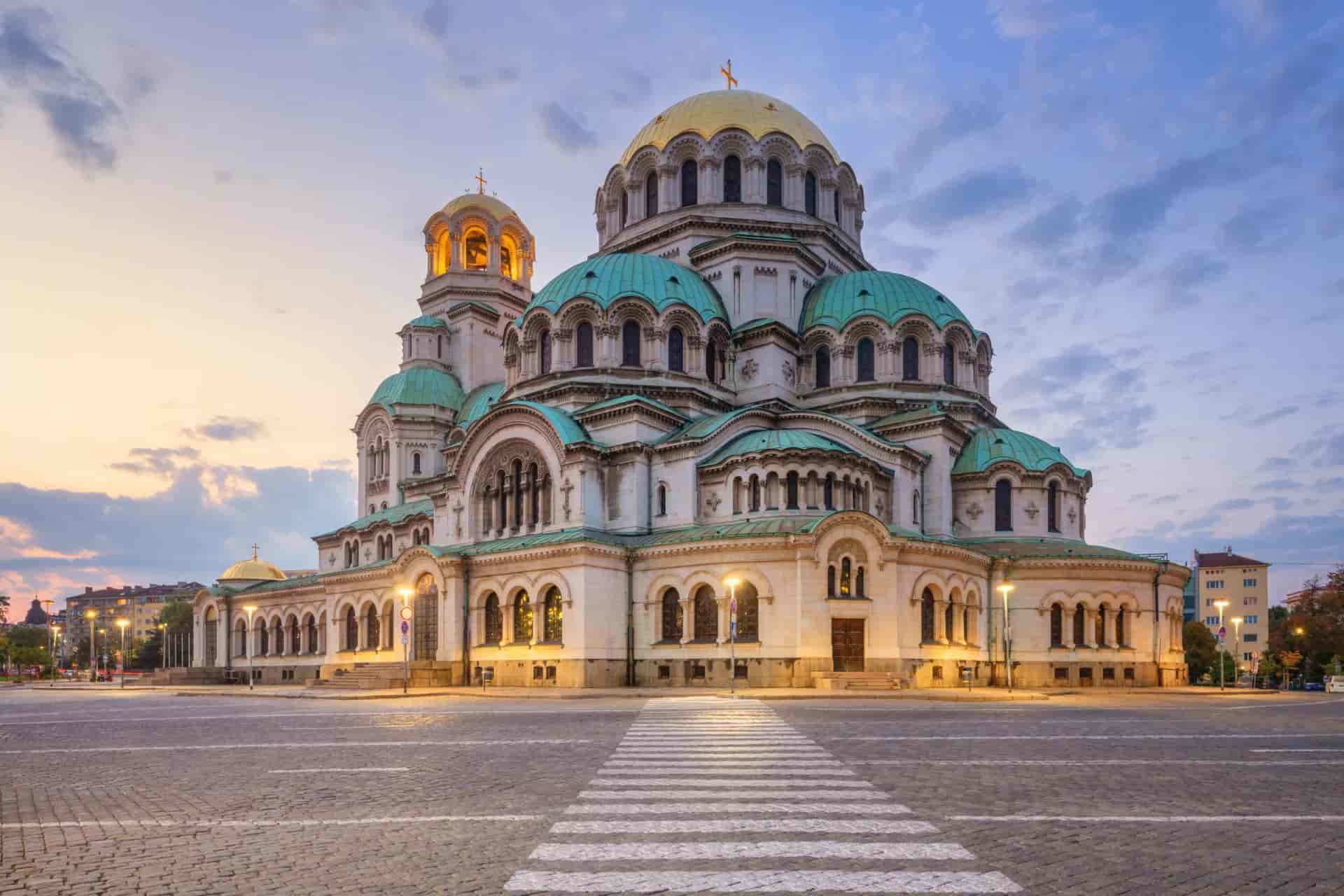 Alexander Nevsky Cathedral in Sofia, Bulgaria, at sunset with golden domes and illuminated facade.