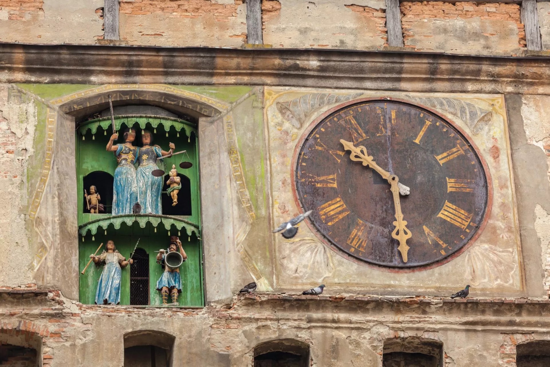Part of the facade of the Clock Tower in Sighisoara, Romania, showing mechanical figures and a rusted clock face.