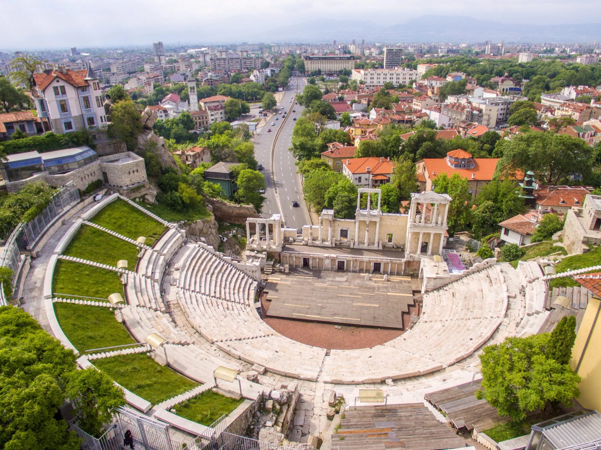 Ancient Roman amphitheater in Plovdiv overlooking a modern city and distant mountains.