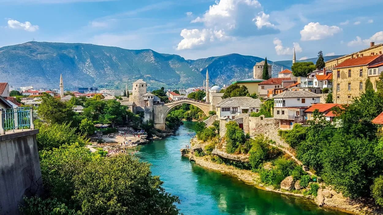 Stari Most bridge over emerald river in Mostar with historic buildings and mountains.