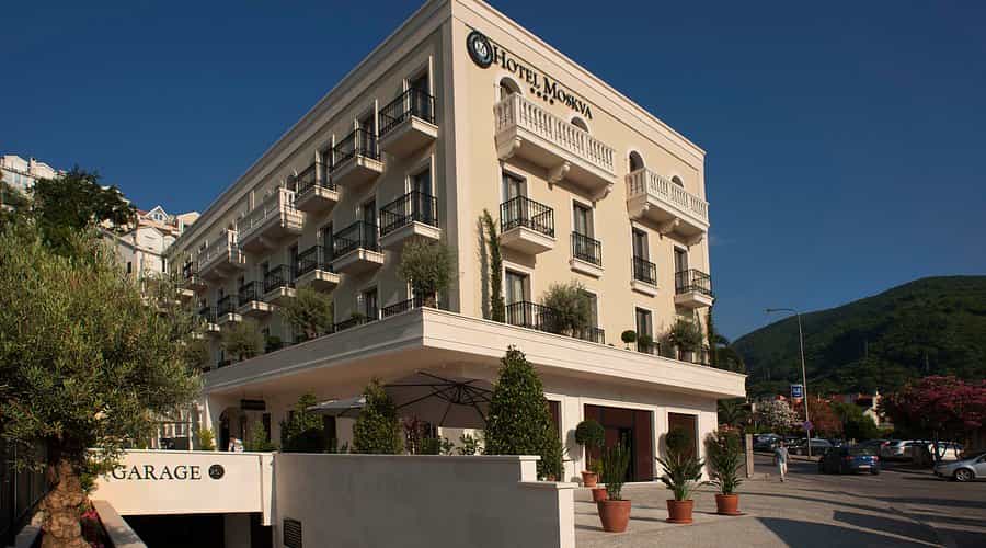 Hotel Moskva in Budva with balconies, potted plants, and a green mountain backdrop.