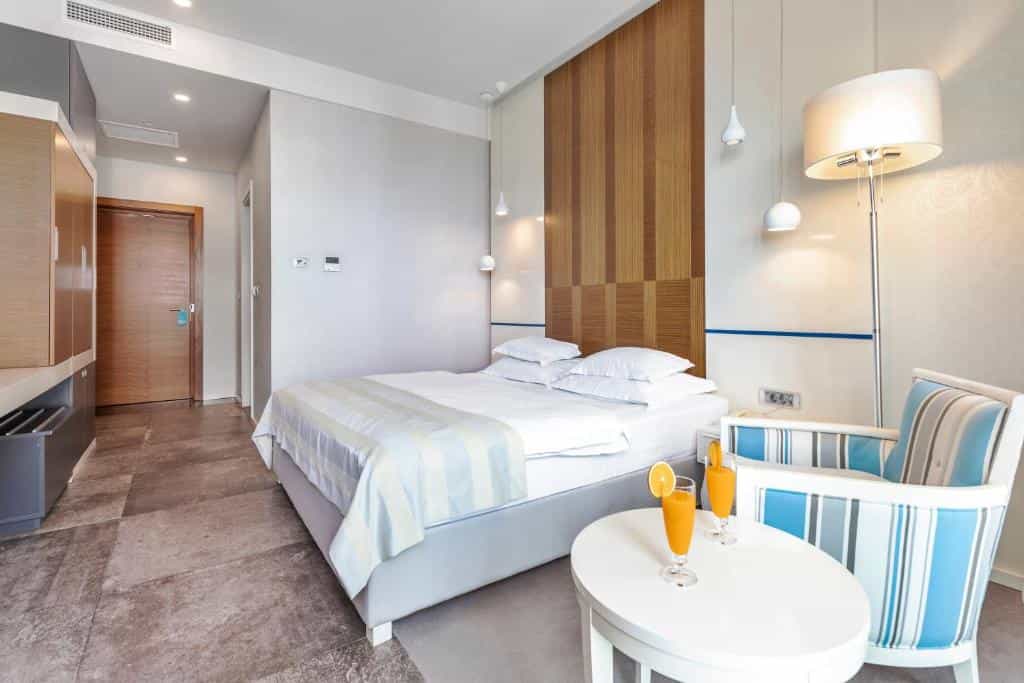 Modern hotel room with white bedding, wood accents, and orange juice on a side table.