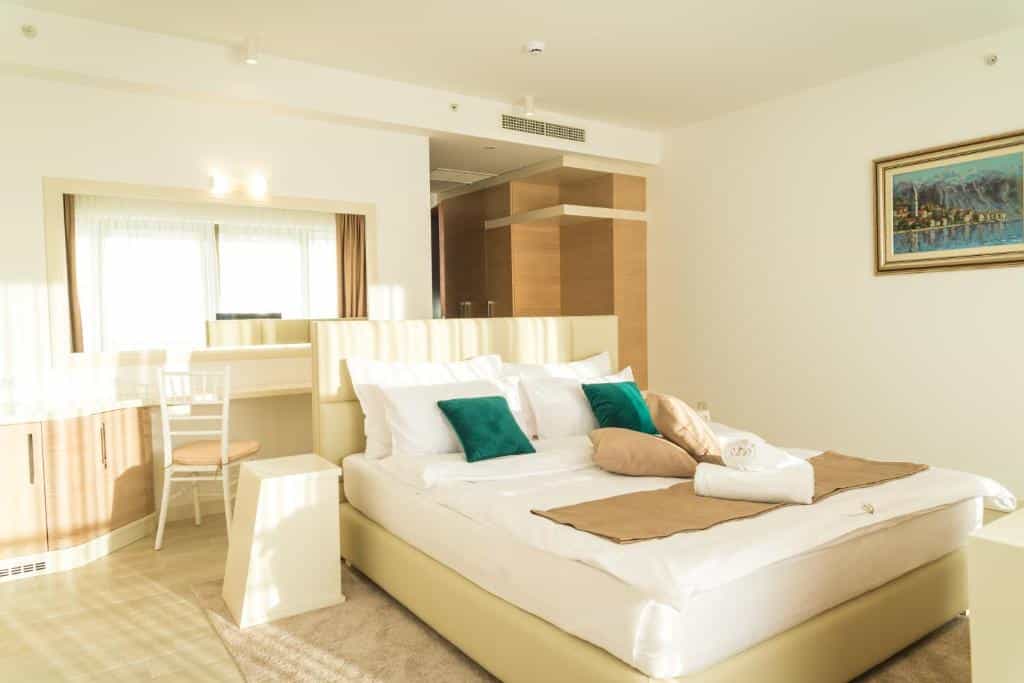 Bright hotel bedroom with large bed, white linens, green pillows, and desk area.