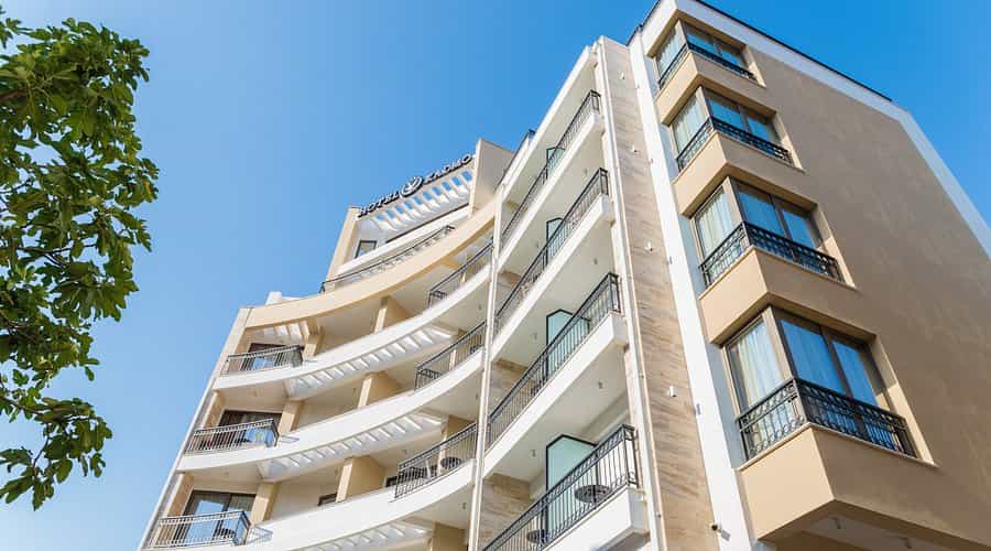 Hotel Kadmo building facade with curved balconies against a clear blue sky, green leaves visible.