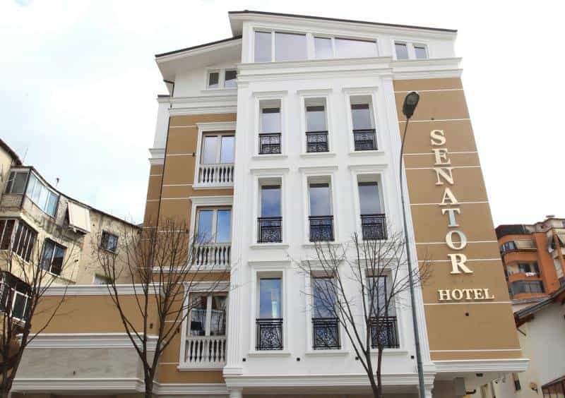 Hotel Senator building facade with white neoclassical trim and tan siding in a city setting.