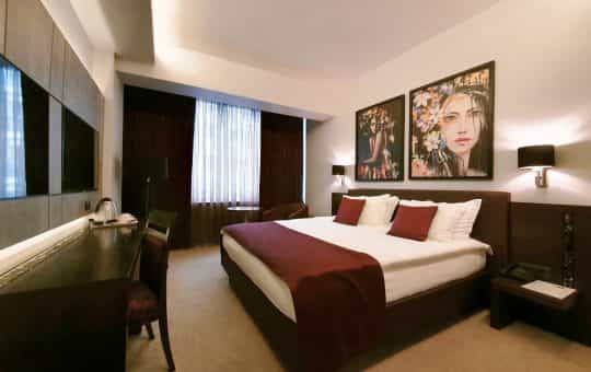 Hotel bedroom with large bed, modern art prints, and dark wood desk area.