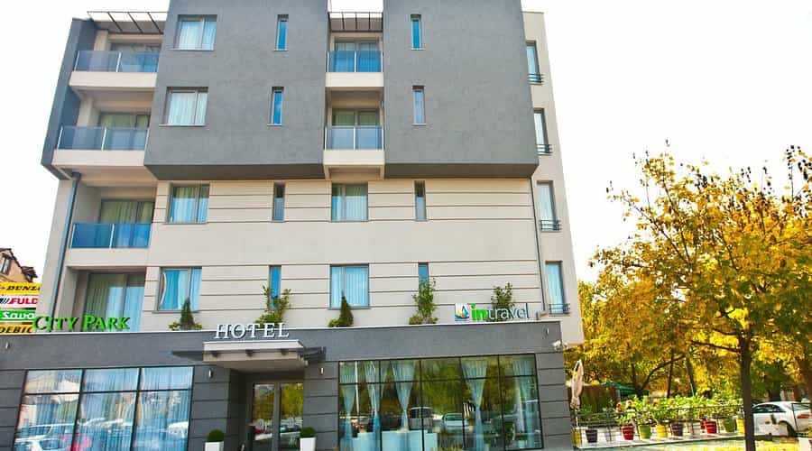 Hotel City Park building exterior with modern gray and beige facade and autumn trees.