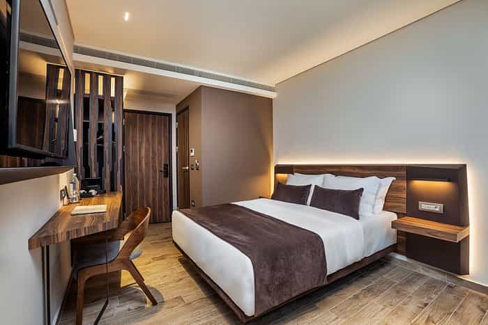 Modern hotel bedroom with wood accents, desk, and backlit headboard in Thessaloniki.