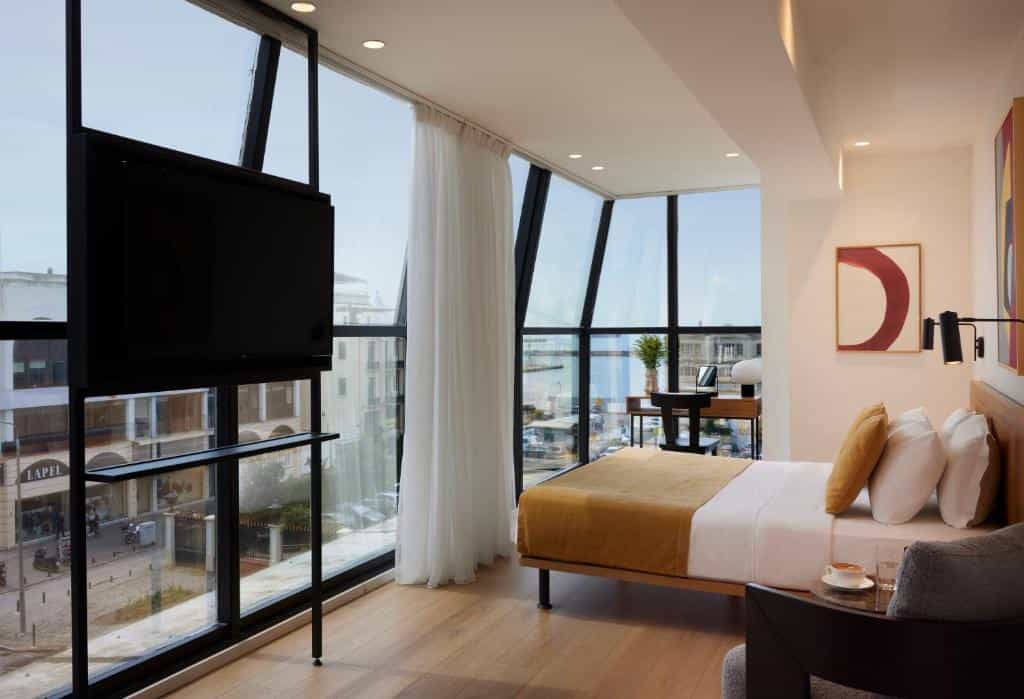 Hotel room with wood floors, large windows, and a bed with yellow and white linens.