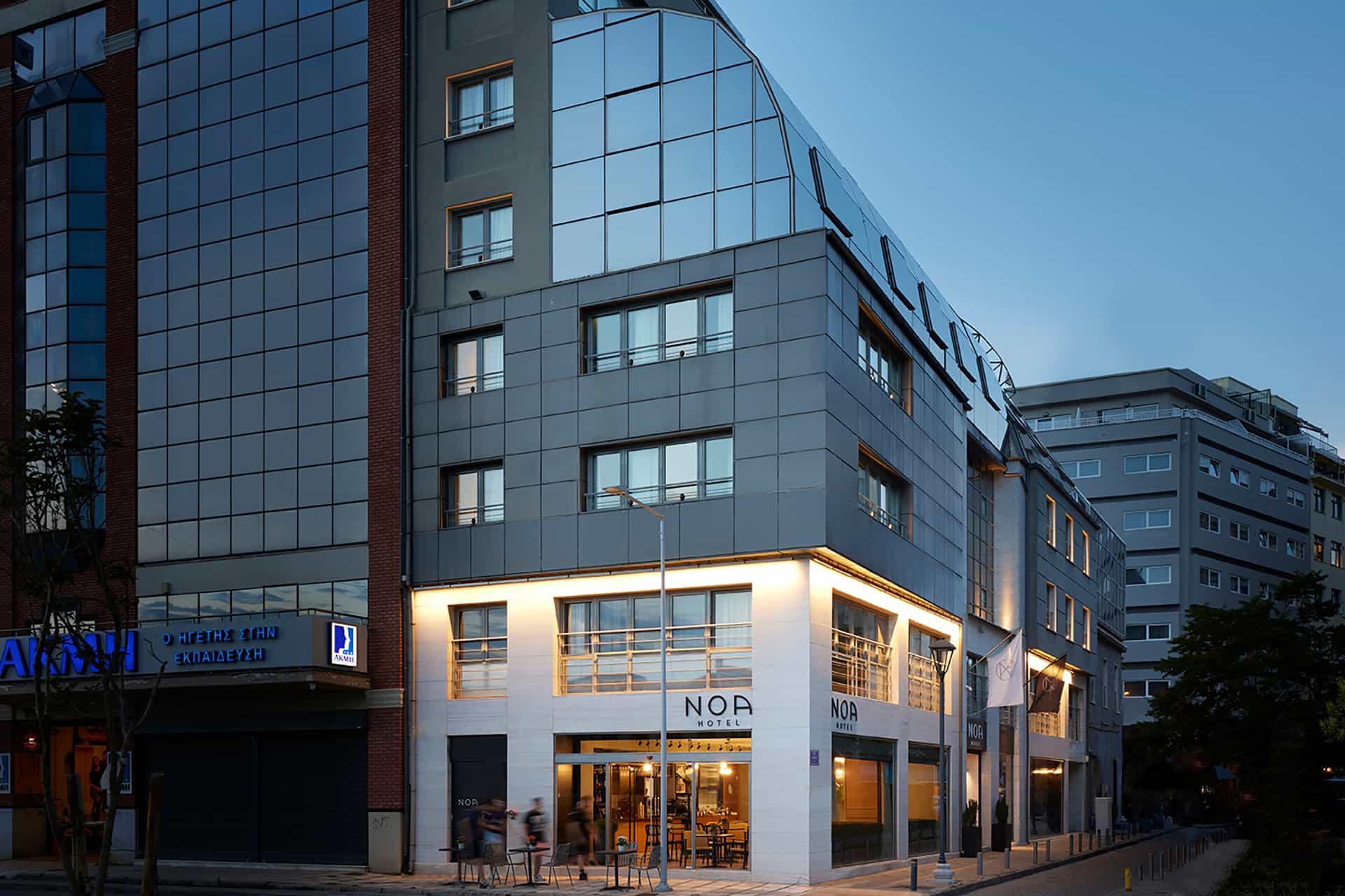 Noa Hotel building exterior at dusk with modern glass and gray paneling in a city setting.
