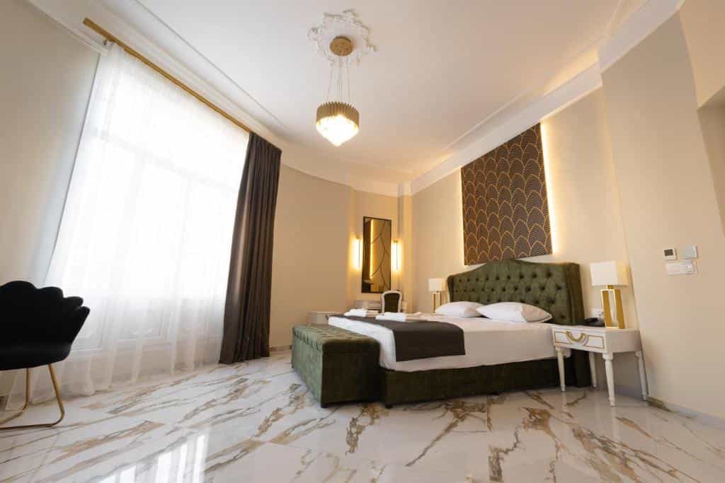 Luxury hotel bedroom with green velvet bed, marble floor, and bright window.