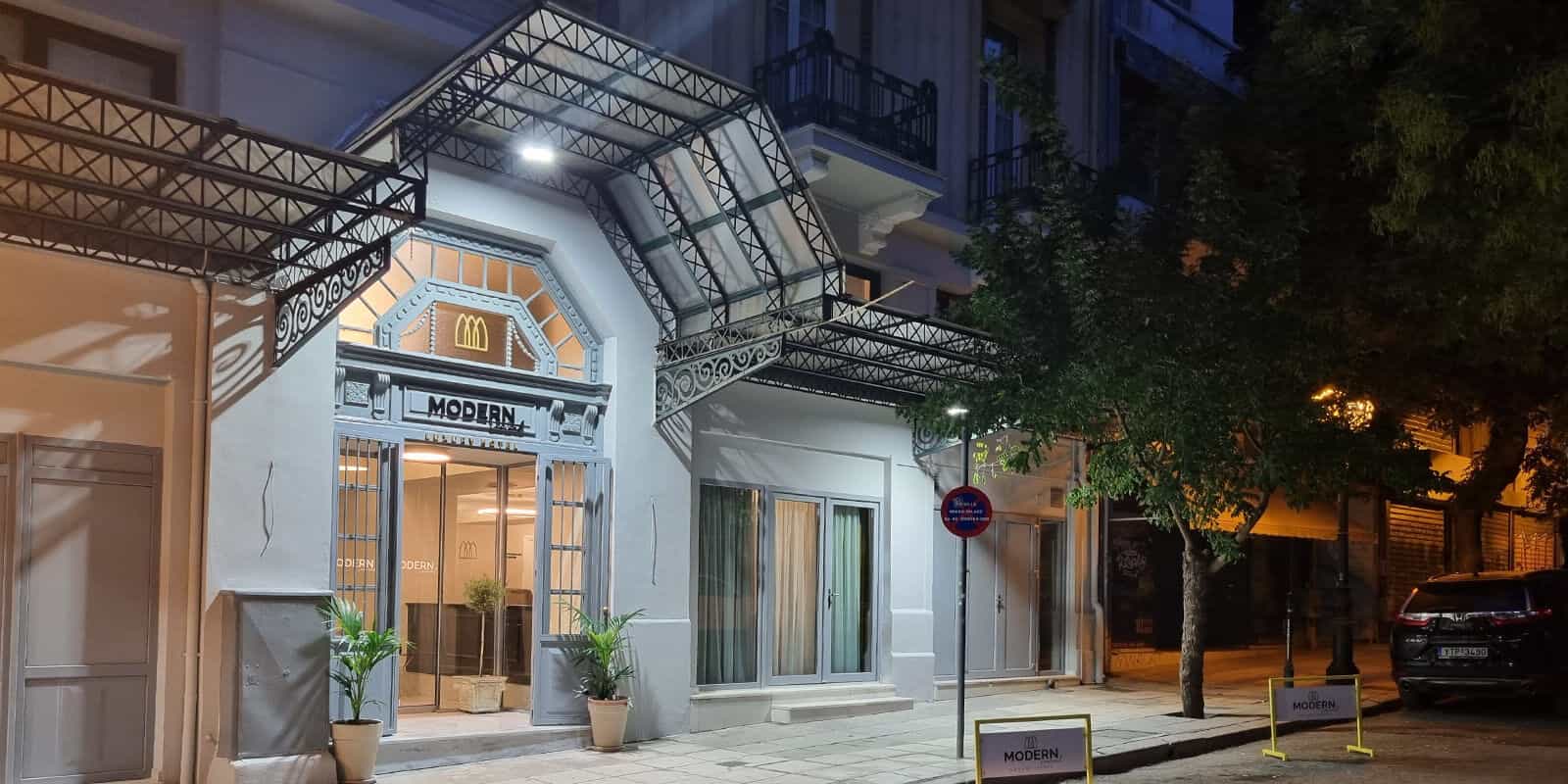 Modern Luxury Hotel entrance at night with ornate metal awning and potted plants.