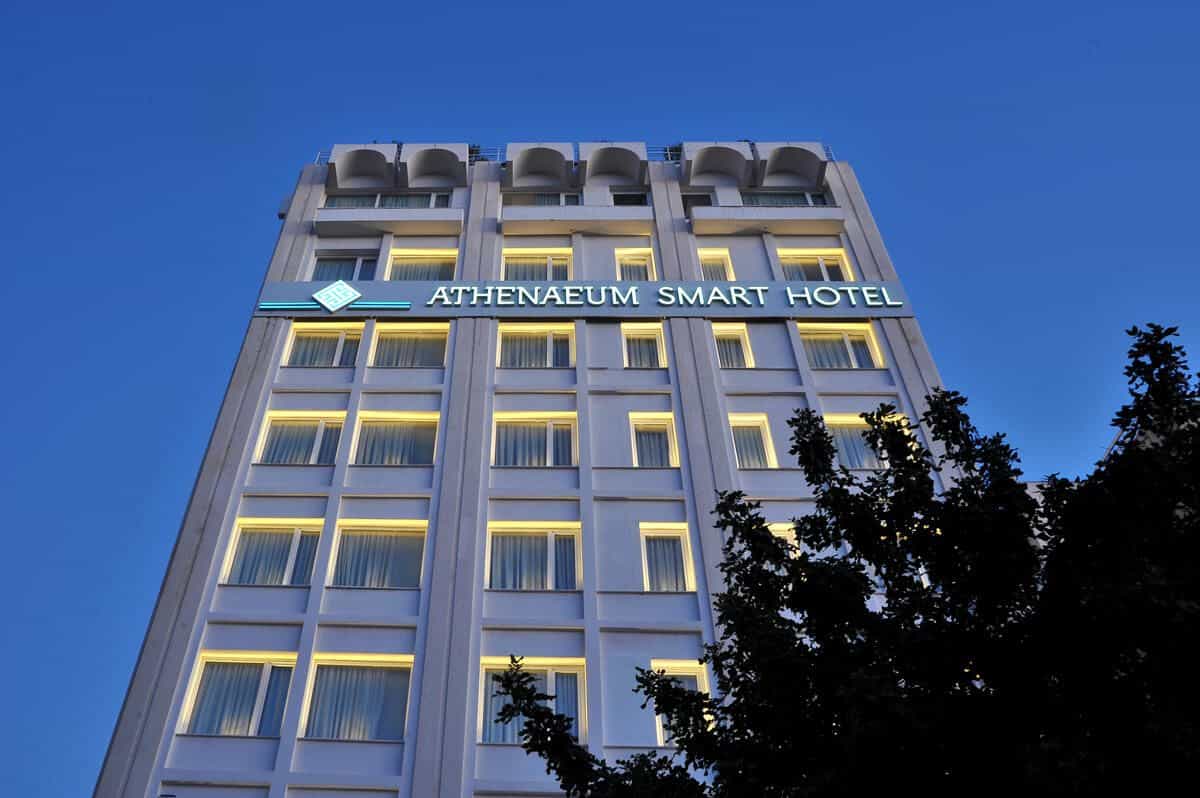 Athenaeum Smart Hotel building facade illuminated against a deep blue twilight sky with tree silhouettes.