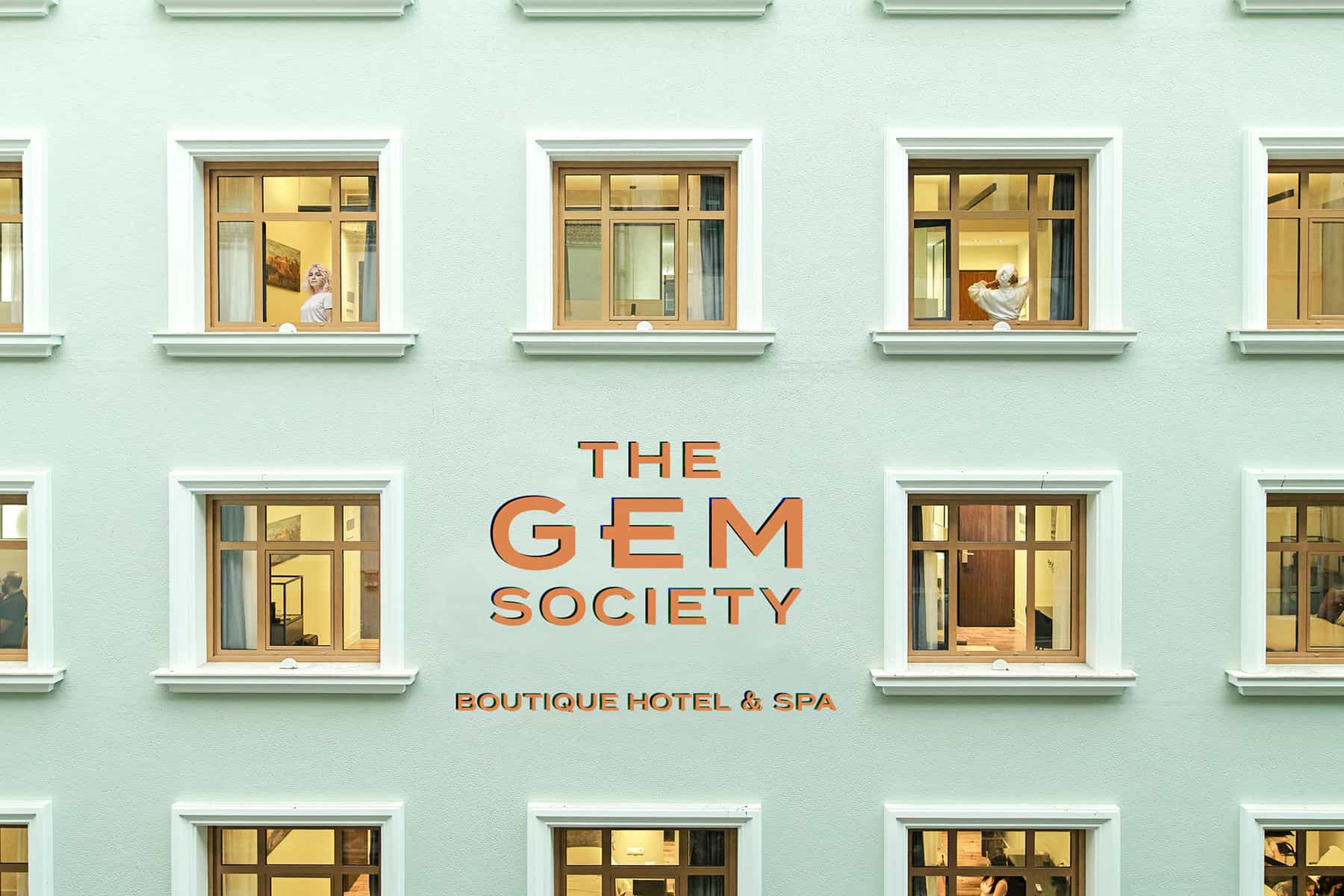 The Gem Society Boutique Hotel & Spa signage on a light green building facade with lit windows.