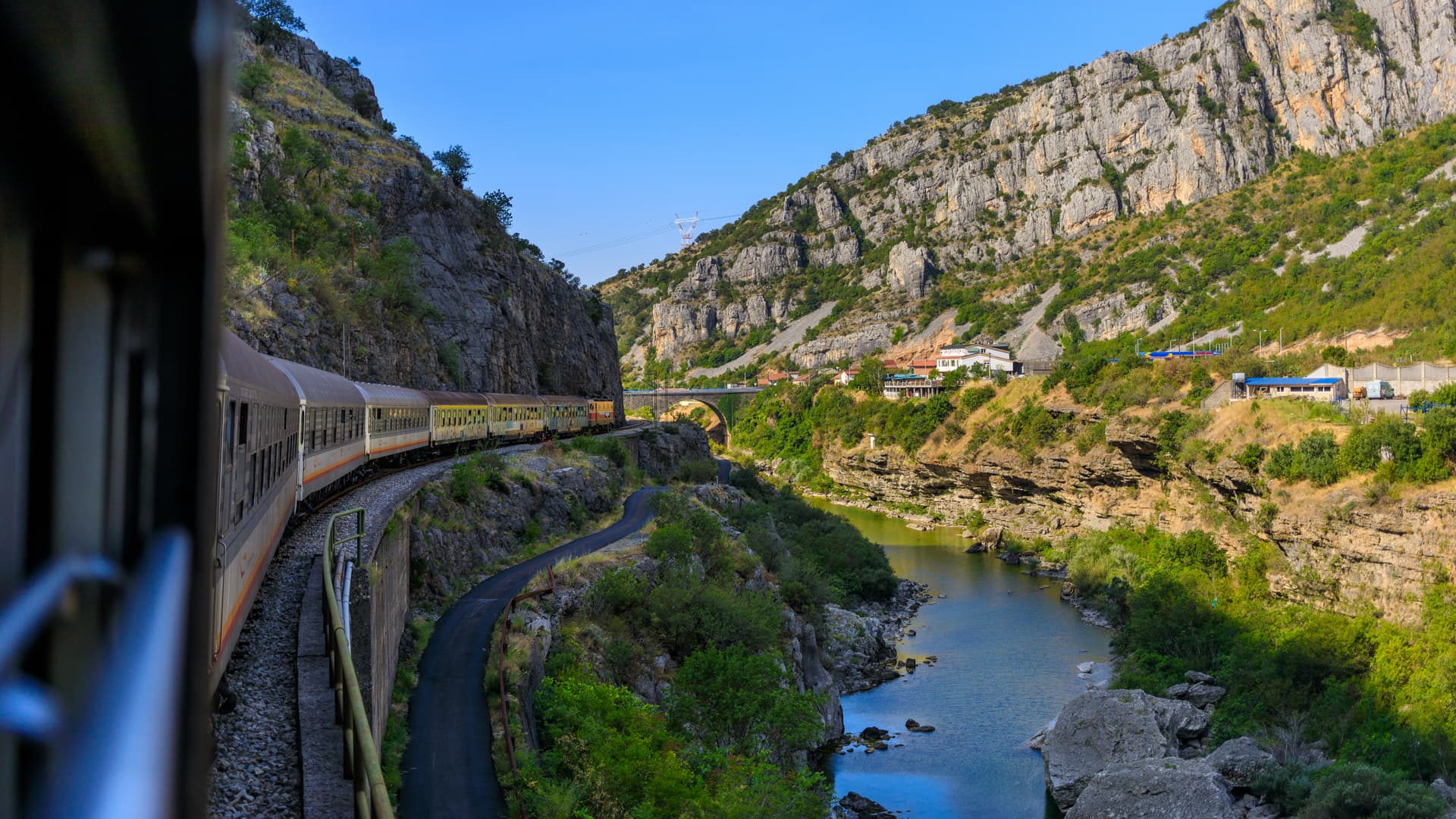 Train curving through a steep mountain canyon alongside a river in Montenegro.