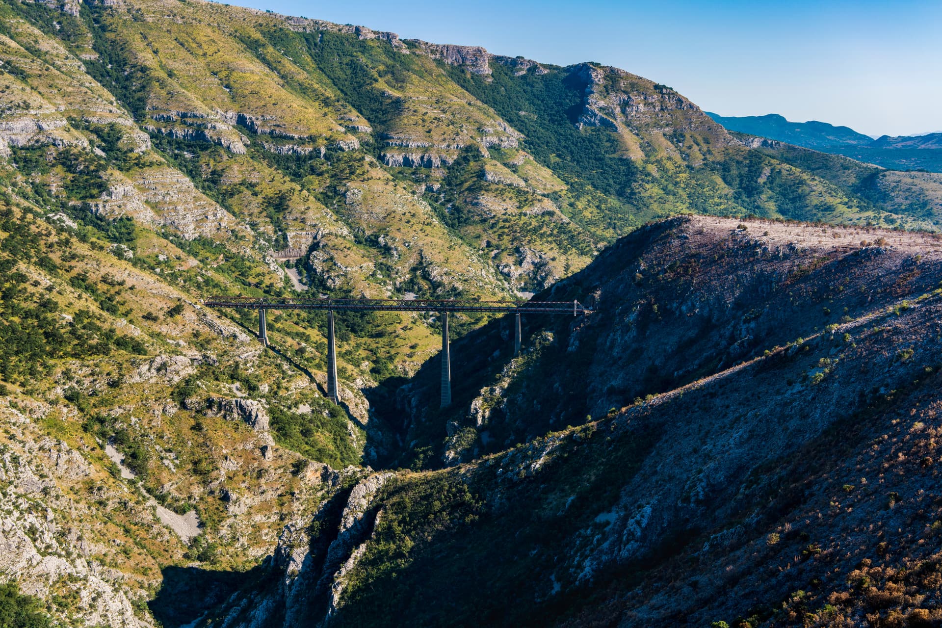 Mala Rijeka viaduct crossing a deep canyon between arid, scrub-covered mountains under a clear blue sky.