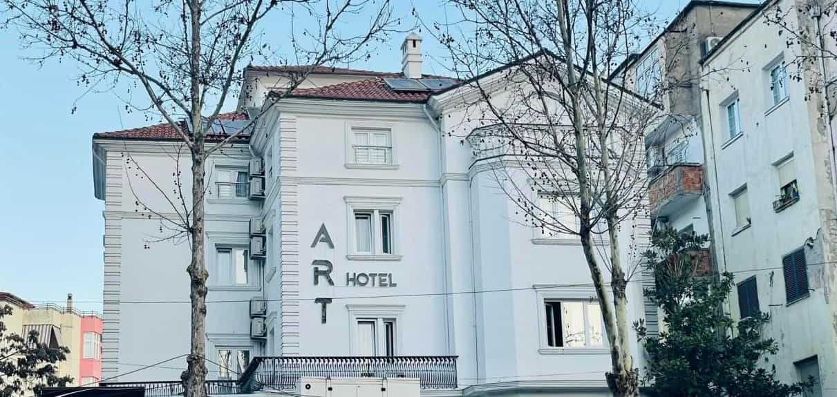 White ART Hotel building facade with bare trees in front under a pale blue sky.