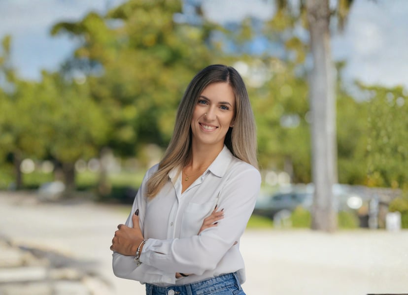 Smiling woman with arms crossed wearing a white button-down shirt outdoors in a park setting.