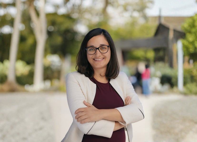 Woman smiling with arms crossed standing in a park setting.