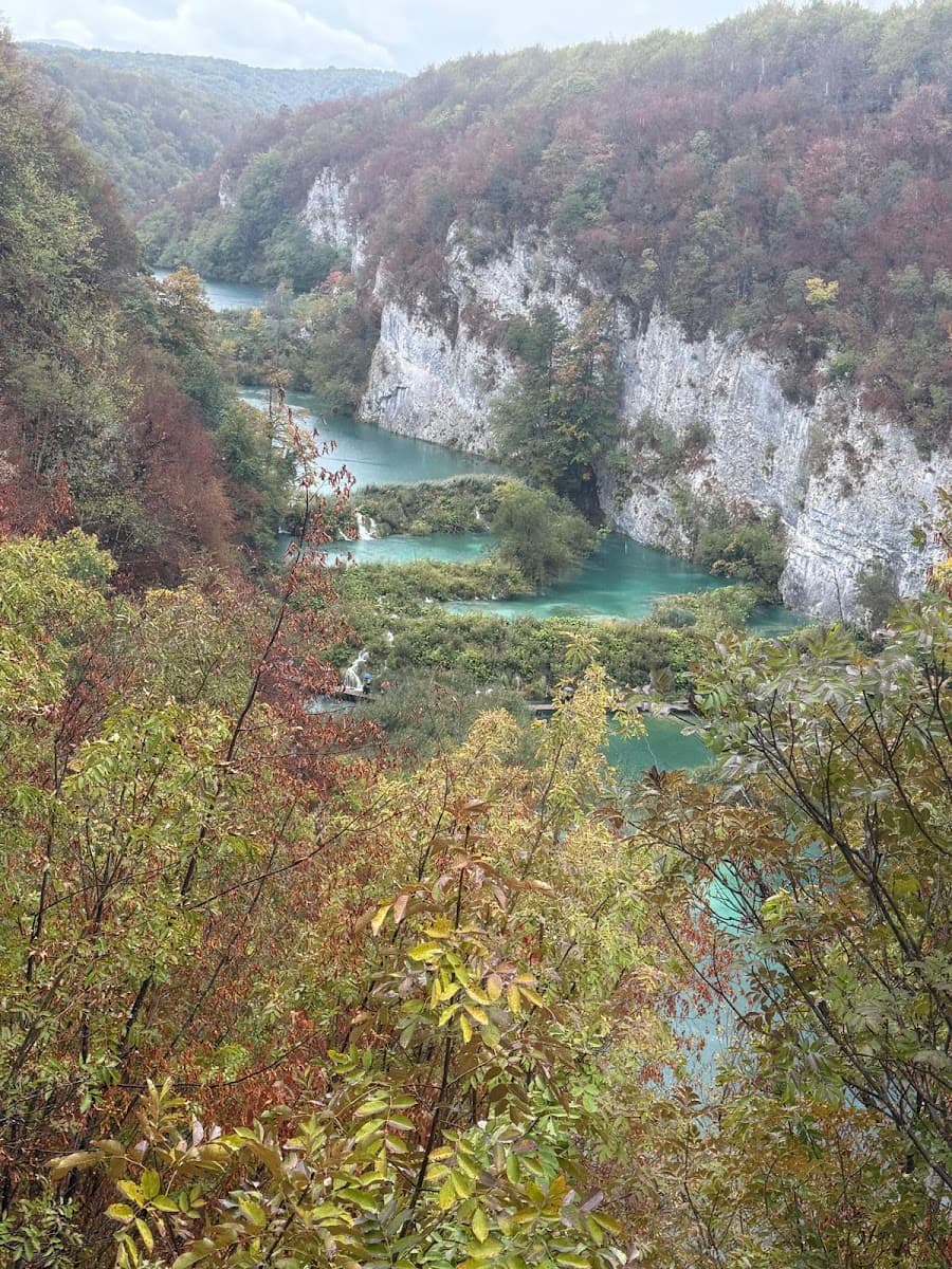 Turquoise lakes and waterfalls flowing through a canyon with autumn foliage and rocky cliffs