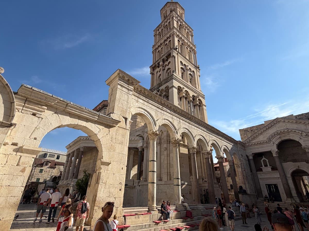 Ancient stone bell tower and colonnade with people walking in historic square